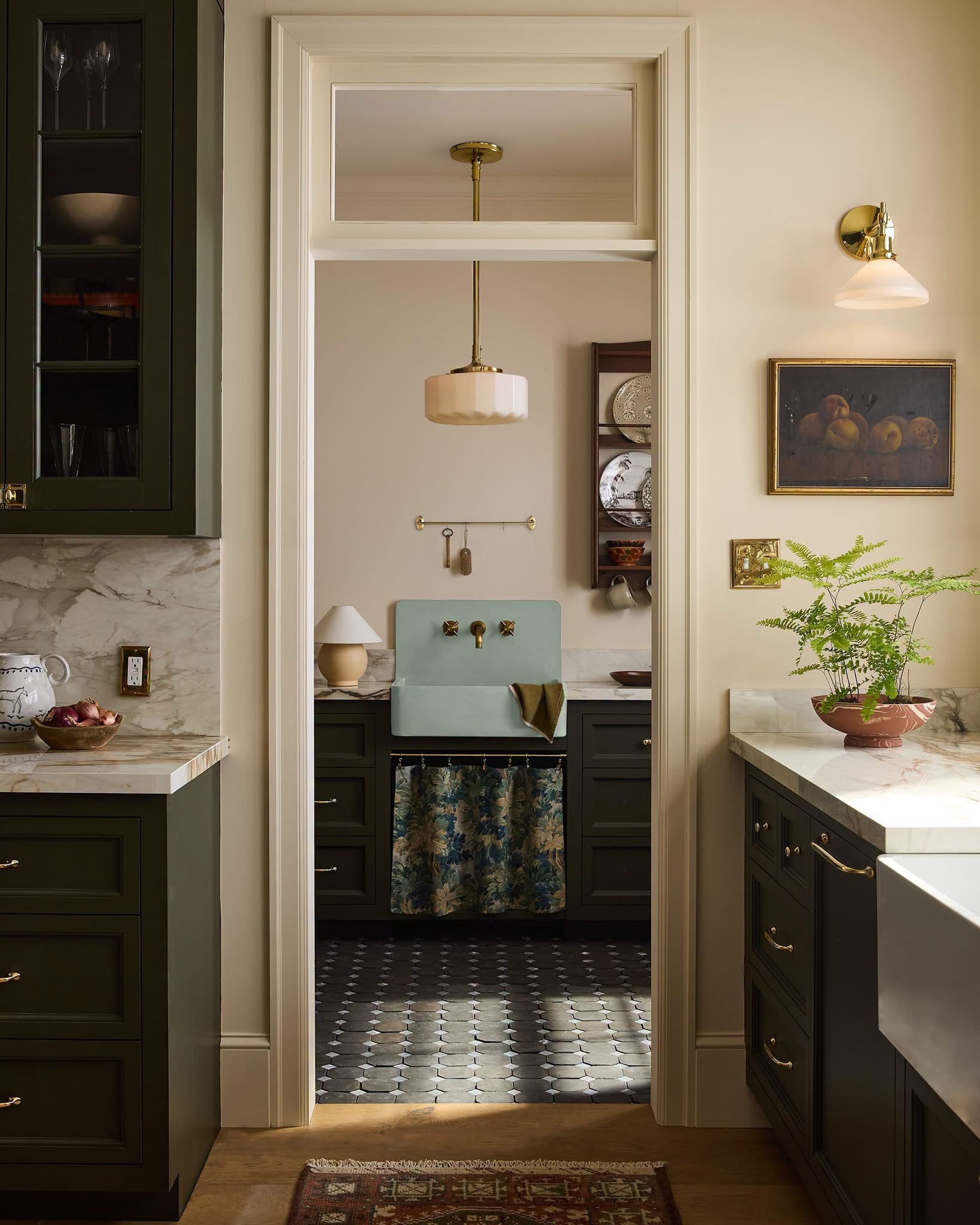 A calm olive kitchen looking into a tidy pantry